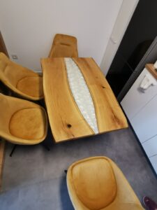 Handcrafted solid wood dining table with a pale inlay center, surrounded by matching wooden chairs in a showroom.