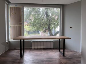 Handcrafted wooden table with black metal legs sits in a bright room by a large window, showcasing premium wooden tables and doors.