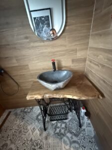 Handcrafted wooden table vanity with a stone basin sink and round mirror, illustrating artisanal wood furniture for stylish bathrooms.