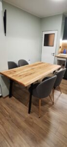 Showroom scene featuring a natural solid-wood dining table with gray upholstered chairs in a pale-green room.