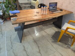 Handcrafted wooden table with dark metal legs in a showroom, with a laptop, water bottles, and yellow chairs nearby, showcasing custom wooden tables and doors.
