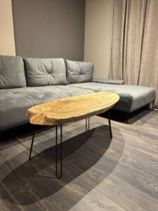 Showroom scene featuring a handcrafted live-edge wooden coffee table with black metal legs beside a gray sectional sofa, showcasing high-quality wooden tables.