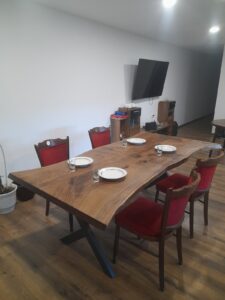 Solid wood dining table with red chairs in a showroom, highlighting custom wooden tables and doors.