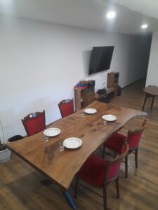 Solid wood dining table with red upholstered chairs set with plates in a showroom, highlighting handcrafted wooden tables and doors for sale.